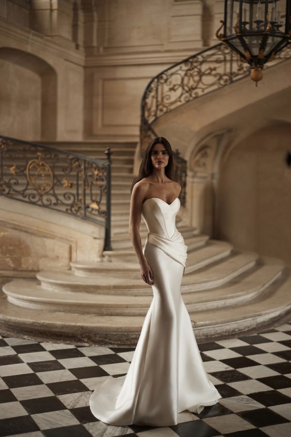 Diane by Milla Nova. Sophisticated mermaid gown in mikado with masterful drapery accentuating the hips. Featuring a heart-shaped neckline with integrated cups, a structured corset, lace-up closure at the back, and a form-fitting mermaid skirt with draping on the hips and a short train.