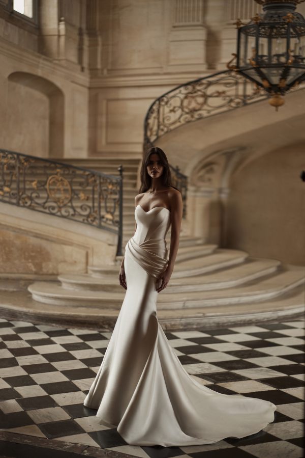 Diane by Milla Nova. A Sophisticated mermaid gown in Mikado with masterful drapery accentuating the hips. Featuring a heart-shaped neckline with integrated cups, a structured corset, a lace-up closure at the back, and a form-fitting mermaid skirt with draping on the hips and a short train.