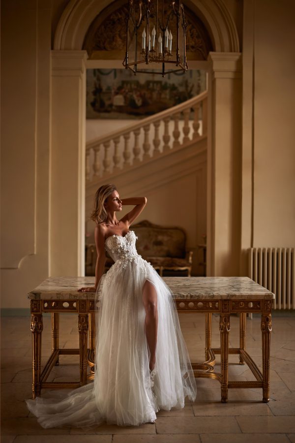 Sinatra by Milla. A Magnificent A-line semi-transparent wedding gown crafted from chantilly lace, delicately sprinkled with 3D flowers and sequins. Boasting a heart-shaped semi-transparent corset with built-in cups, adorned with 3D floral appliqués and sequins, a zip closure on the back, and a voluminous tulle