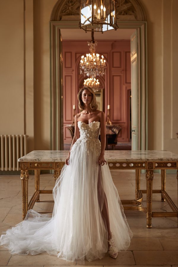 Sinatra by Milla. A Magnificent A-line semi-transparent wedding gown crafted from chantilly lace, delicately sprinkled with 3D flowers and sequins. Boasting a heart-shaped semi-transparent corset with built-in cups, adorned with 3D floral appliqués and sequins, a zip closure on the back, and a voluminous tulle skirt over chantilly lace.