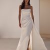 Sandal by Milla Nova. A Refined fitted wedding gown cut from satin fabric. Featuring a geometric neckline, lace-up or zipper closure on the back, and a beautifully draped waist that gracefully transitions into a gorgeous layering skirt with a delicate train.