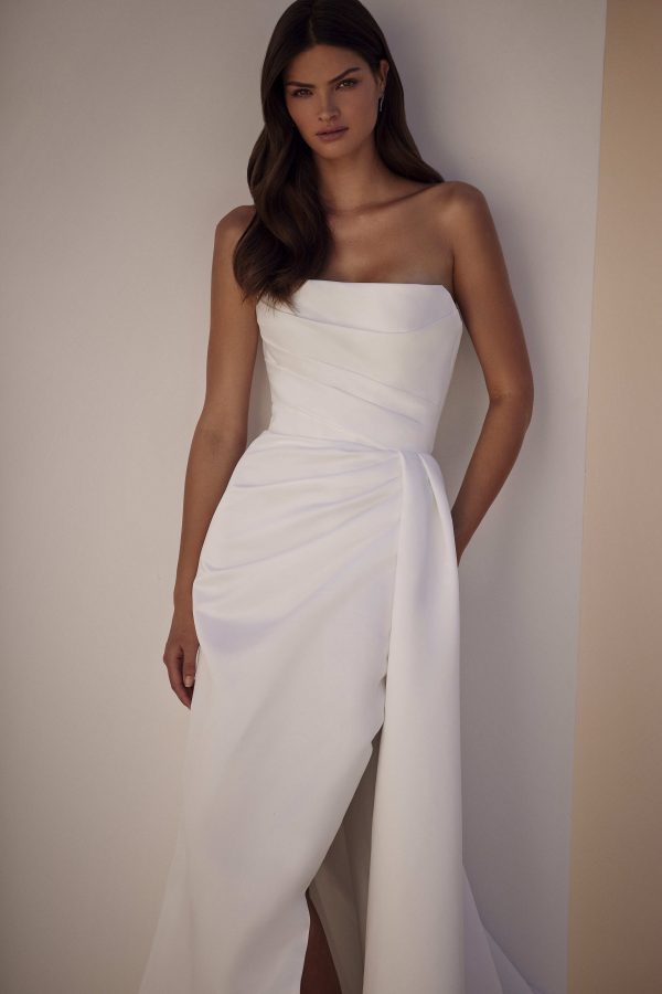 Sandal by Milla Nova. A Refined fitted wedding gown cut from satin fabric. Featuring a geometric neckline, lace-up or zipper closure on the back, and a beautifully draped waist that gracefully transitions into a gorgeous layering skirt with a delicate train.