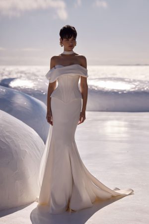 Floriane by Milla Nova. A sleek and chic wedding corset with a structured, boned design that enhances the silhouette. Featuring a heart-shaped neckline and oversized draped off-the-shoulder sleeves sculpted to perfection with a lace-up closure at the back. A sleek and elegant satin mermaid skirt that beautifully hugs the figure, enhancing feminine curves. Made from high-quality satin, it provides a luxurious sheen and smooth texture. The fitted silhouette flares out gracefully from the knee, creating a sophisticated and timeless look.