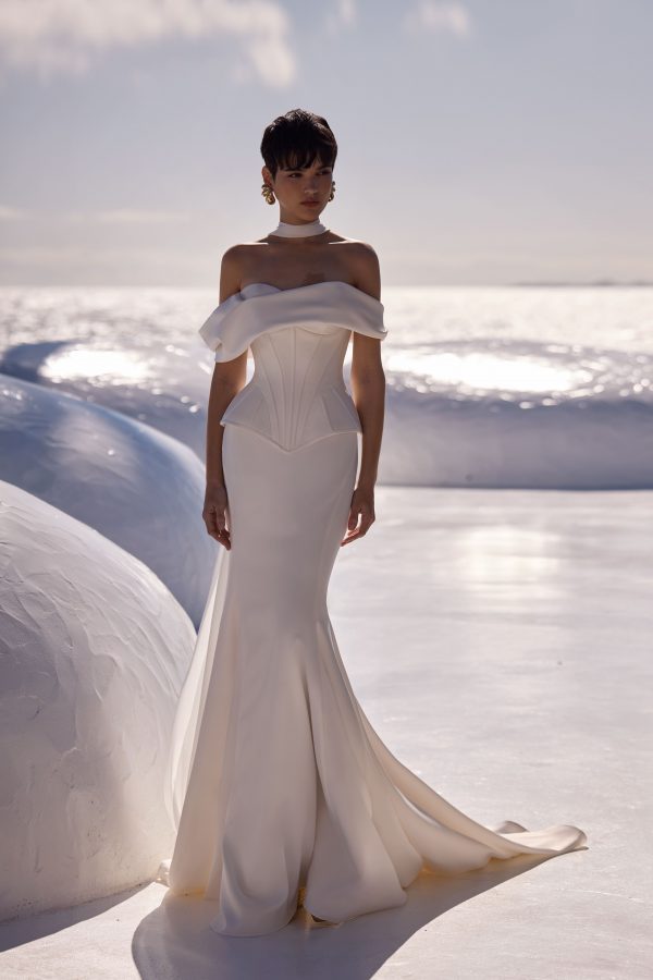 Floriane by Milla Nova. A sleek and chic wedding corset with a structured, boned design that enhances the silhouette. Featuring a heart-shaped neckline and oversized draped off-the-shoulder sleeves sculpted to perfection with a lace-up closure at the back. A sleek and elegant satin mermaid skirt that beautifully hugs the figure, enhancing feminine curves. Made from high-quality satin, it provides a luxurious sheen and smooth texture. The fitted silhouette flares out gracefully from the knee, creating a sophisticated and timeless look.