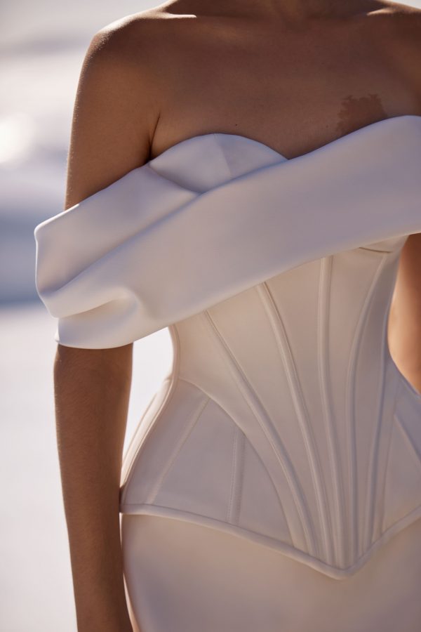 Floriane by Milla Nova. A sleek and chic wedding corset with a structured, boned design that enhances the silhouette. Featuring a heart-shaped neckline and oversized draped off-the-shoulder sleeves sculpted to perfection with a lace-up closure at the back. A sleek and elegant satin mermaid skirt that beautifully hugs the figure, enhancing feminine curves. Made from high-quality satin, it provides a luxurious sheen and smooth texture. The fitted silhouette flares out gracefully from the knee, creating a sophisticated and timeless look.
