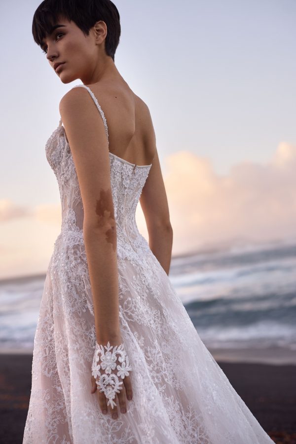 Opal by Milla Nova. A Romantic A-line wedding gown crafted from delicate lace with intricate floral detailing and sparkling all-over sequins. Featuring a boned drop-waist semi-sheer lace corset that flatters the figure, a heart-shaped neckline with subtle V-cut and detachable cups, embellished spaghetti straps, and a closed back with a zip closure. The maxi skirt, made from layers of lace with a nude underskirt, flows gracefully into a midi train, adding an ethereal finish. 
The gown can be elevated with an Opal fingerless gloves.