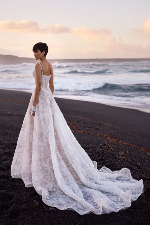 Opal by Milla Nova. A Romantic A-line wedding gown crafted from delicate lace with intricate floral detailing and sparkling all-over sequins. Featuring a boned drop-waist semi-sheer lace corset that flatters the figure, a heart-shaped neckline with subtle V-cut and detachable cups, embellished spaghetti straps, and a closed back with a zip closure. The maxi skirt, made from layers of lace with a nude underskirt, flows gracefully into a midi train, adding an ethereal finish. 
The gown can be elevated with an Opal fingerless gloves.