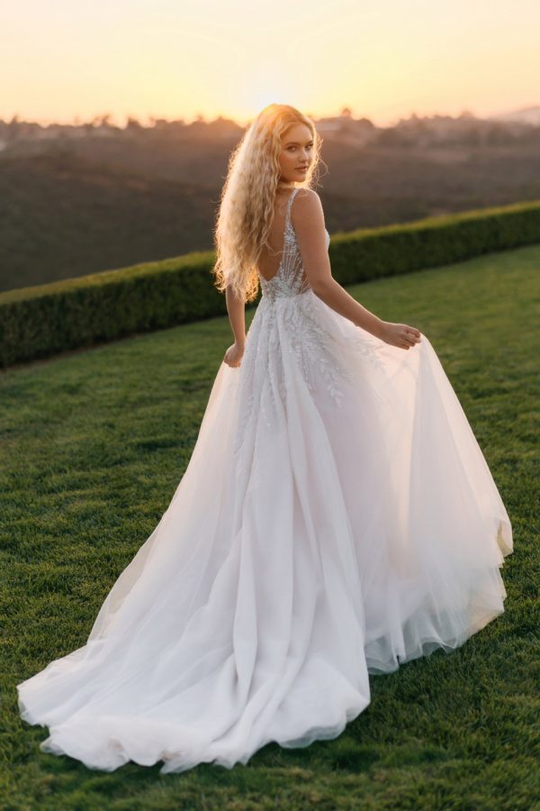 Radiant and graceful, this A-line gown features pearl, beaded, and embroidered lace appliques that glisten over layers of sparkle tulle. The V-neckline and slender straps create a flattering, open frame, while the natural waist flows into a soft, sweeping skirt. With its gentle shimmer and intricate lacework, this gown captures a beautifully romantic sensibility with just the right touch of light-catching detail.